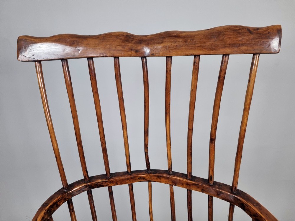 A primitive 18th-century Welsh stick armchair made from dark polished wood featuring a comb back, tapered stick spindles, and an organic curved frame. View VIII