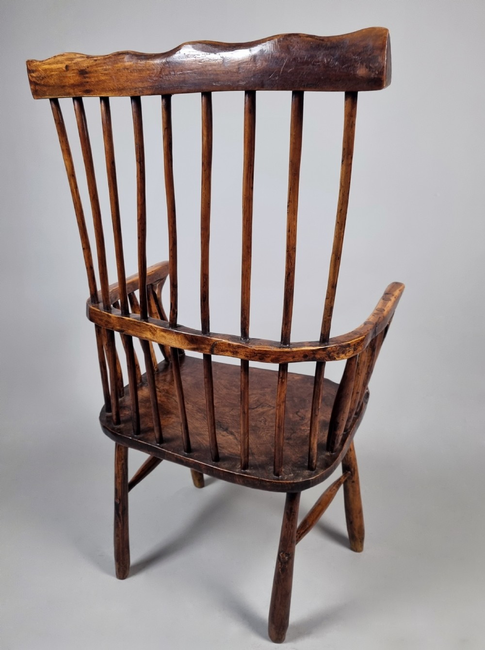 A primitive 18th-century Welsh stick armchair made from dark polished wood featuring a comb back, tapered stick spindles, and an organic curved frame. View IX