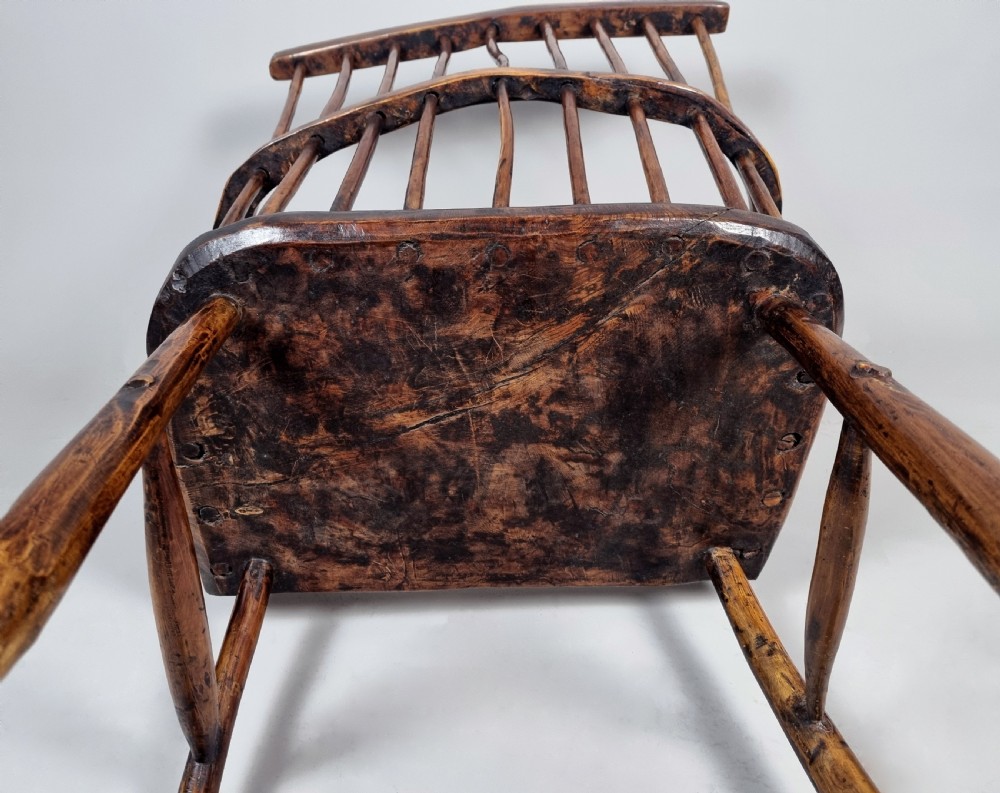 A primitive 18th-century Welsh stick armchair made from dark polished wood featuring a comb back, tapered stick spindles, and an organic curved frame. View X