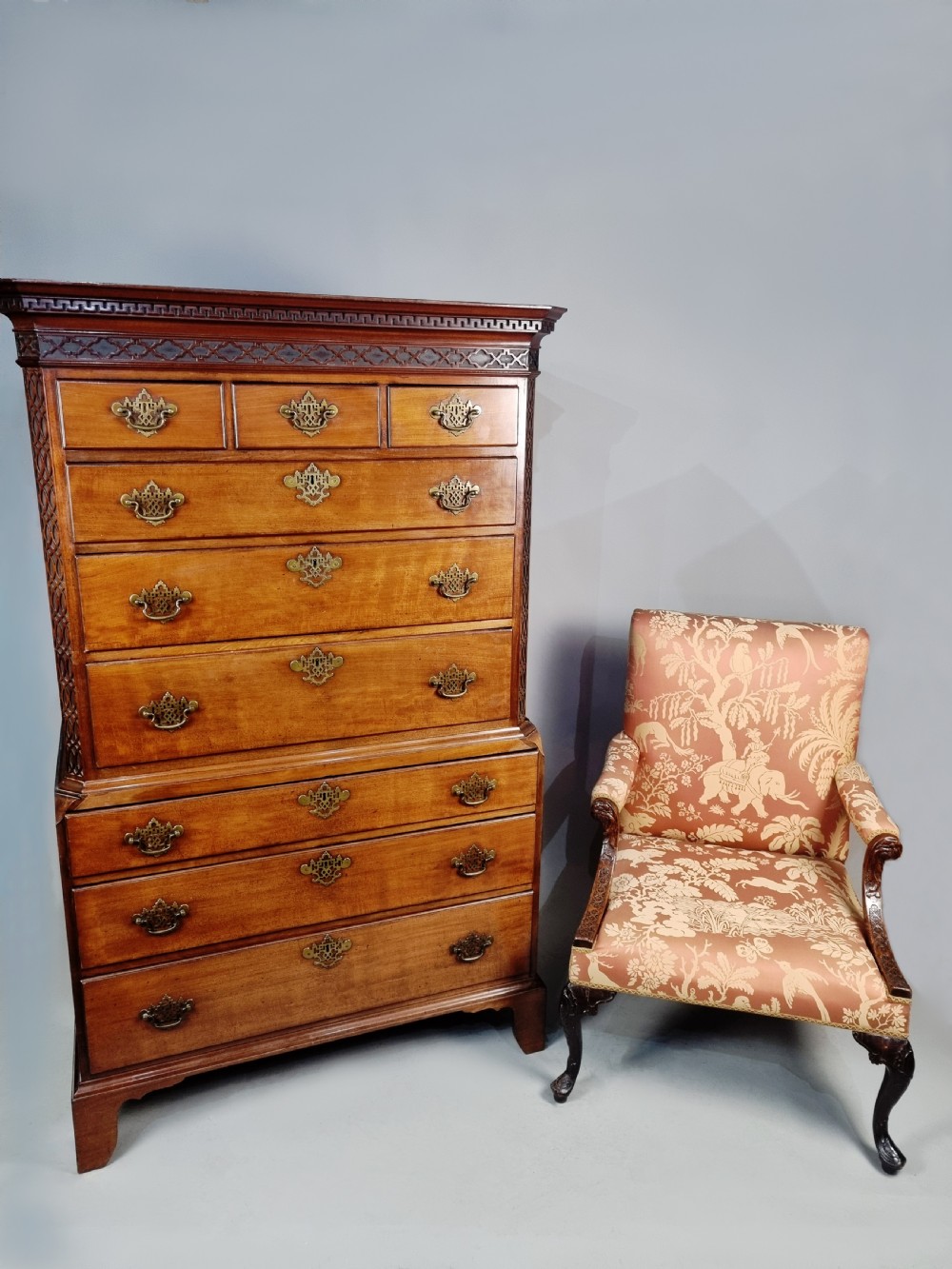 A tall George III mahogany chest on chest featuring stacked drawer sections, pierced brass handles, carved fretwork at the frieze, and bracket feet. View II