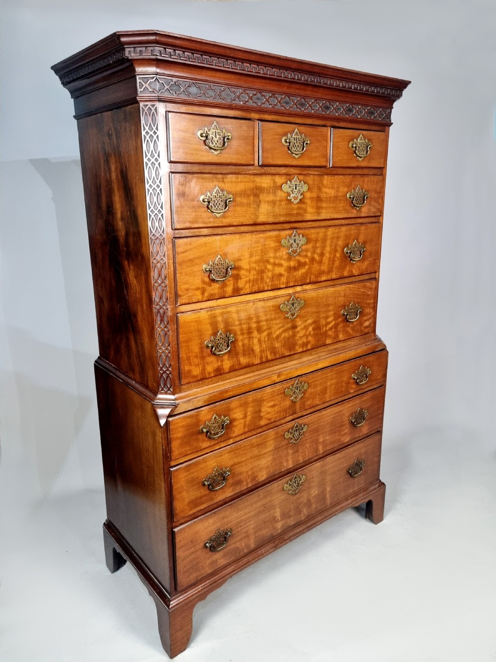 A tall George III mahogany chest on chest featuring stacked drawer sections, pierced brass handles, carved fretwork at the frieze, and bracket feet. View III