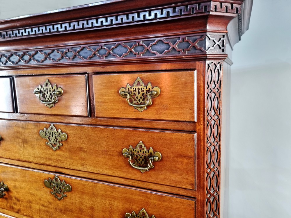 A tall George III mahogany chest on chest featuring stacked drawer sections, pierced brass handles, carved fretwork at the frieze, and bracket feet. View IV