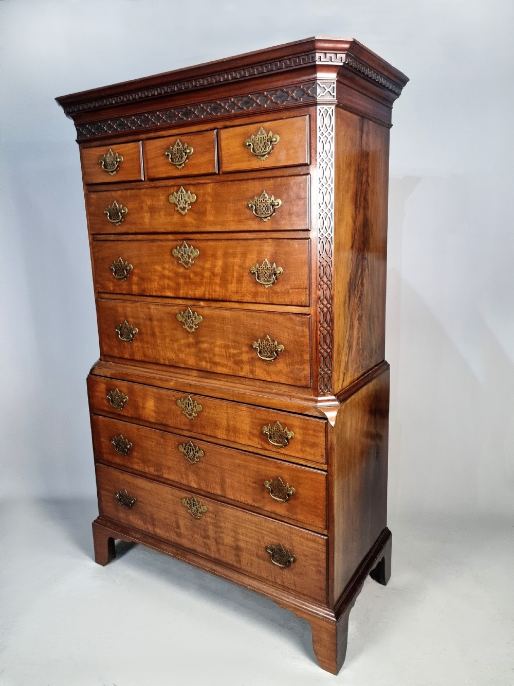 A tall George III mahogany chest on chest featuring stacked drawer sections, pierced brass handles, carved fretwork at the frieze, and bracket feet. View VIII