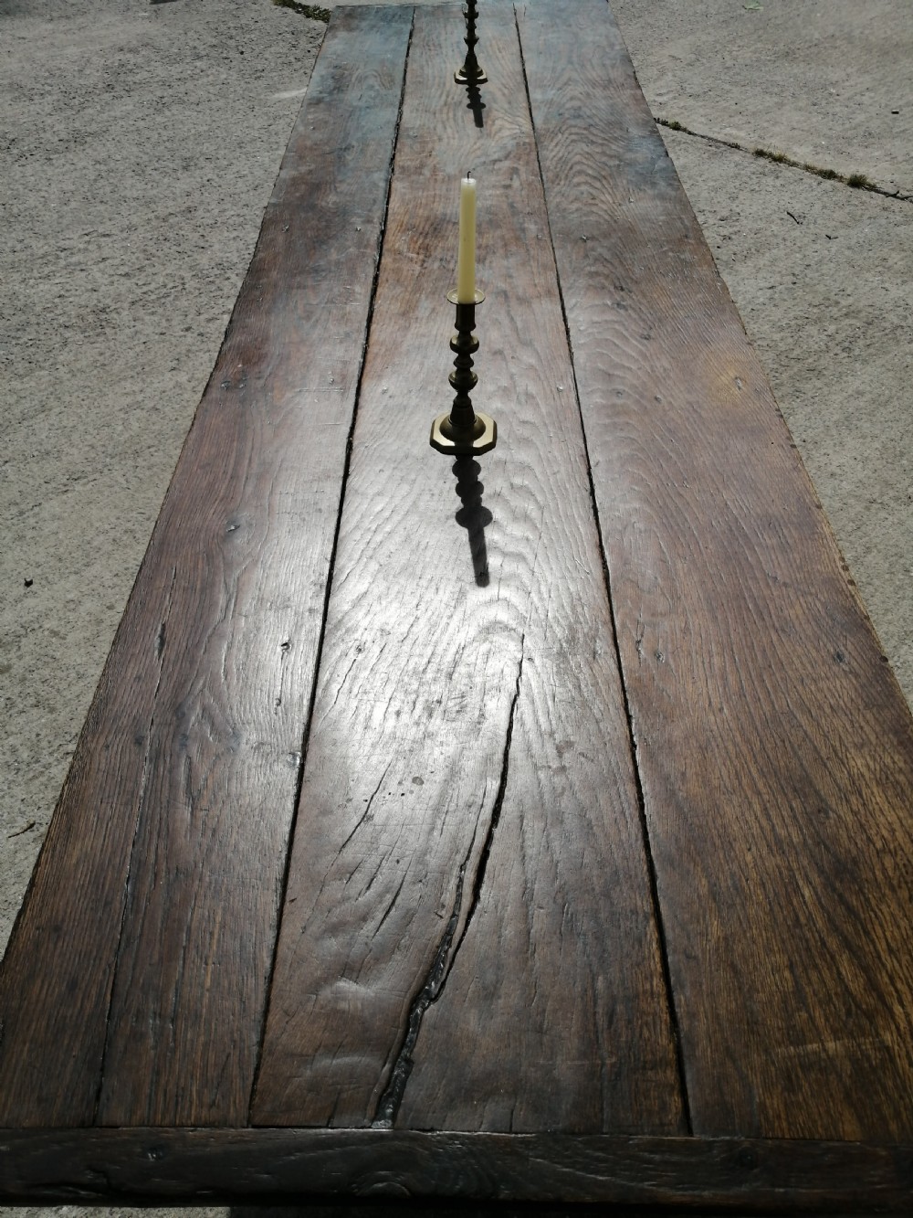 An early eighteenth-century long oak and elm refectory table top showing four wide wooden planks with natural grain, splits, and deep dark patination.