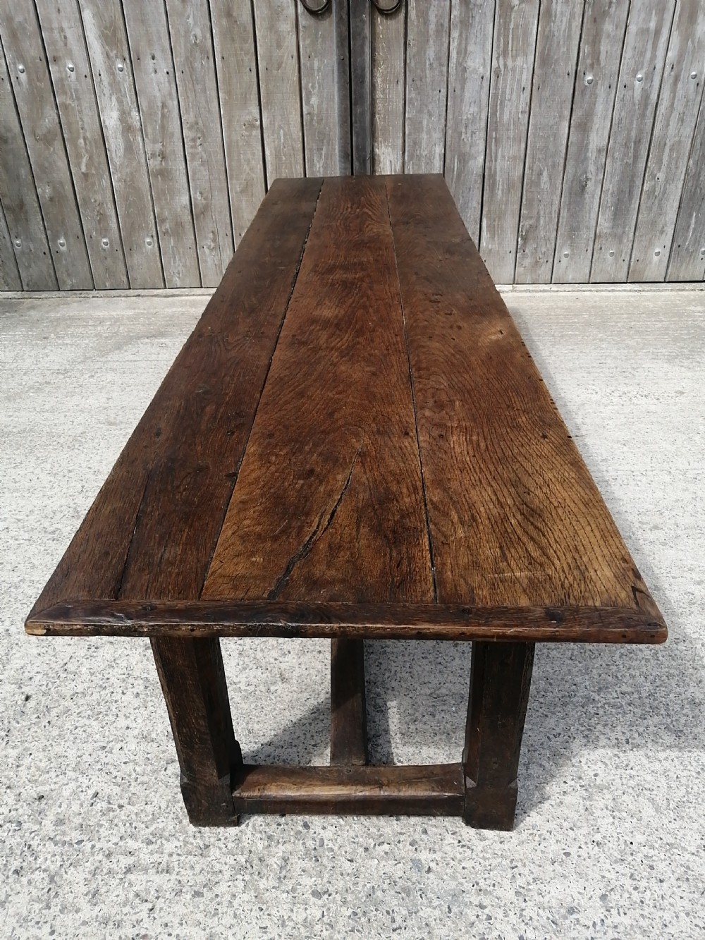 An early eighteenth-century long oak and elm refectory table top showing four wide wooden planks with natural grain, splits, and deep dark patination. View VII
