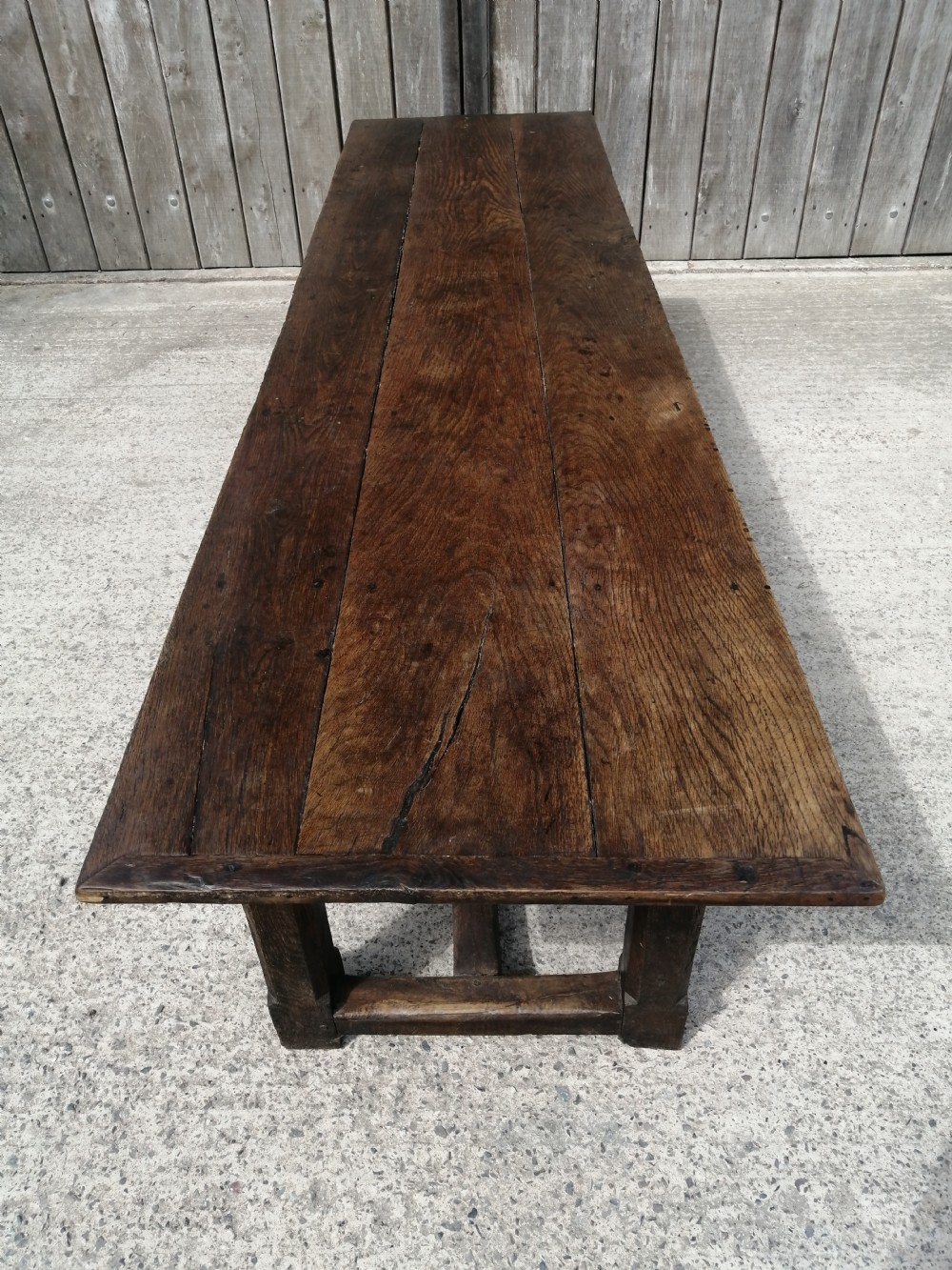 An early eighteenth-century long oak and elm refectory table top showing four wide wooden planks with natural grain, splits, and deep dark patination. View VIII