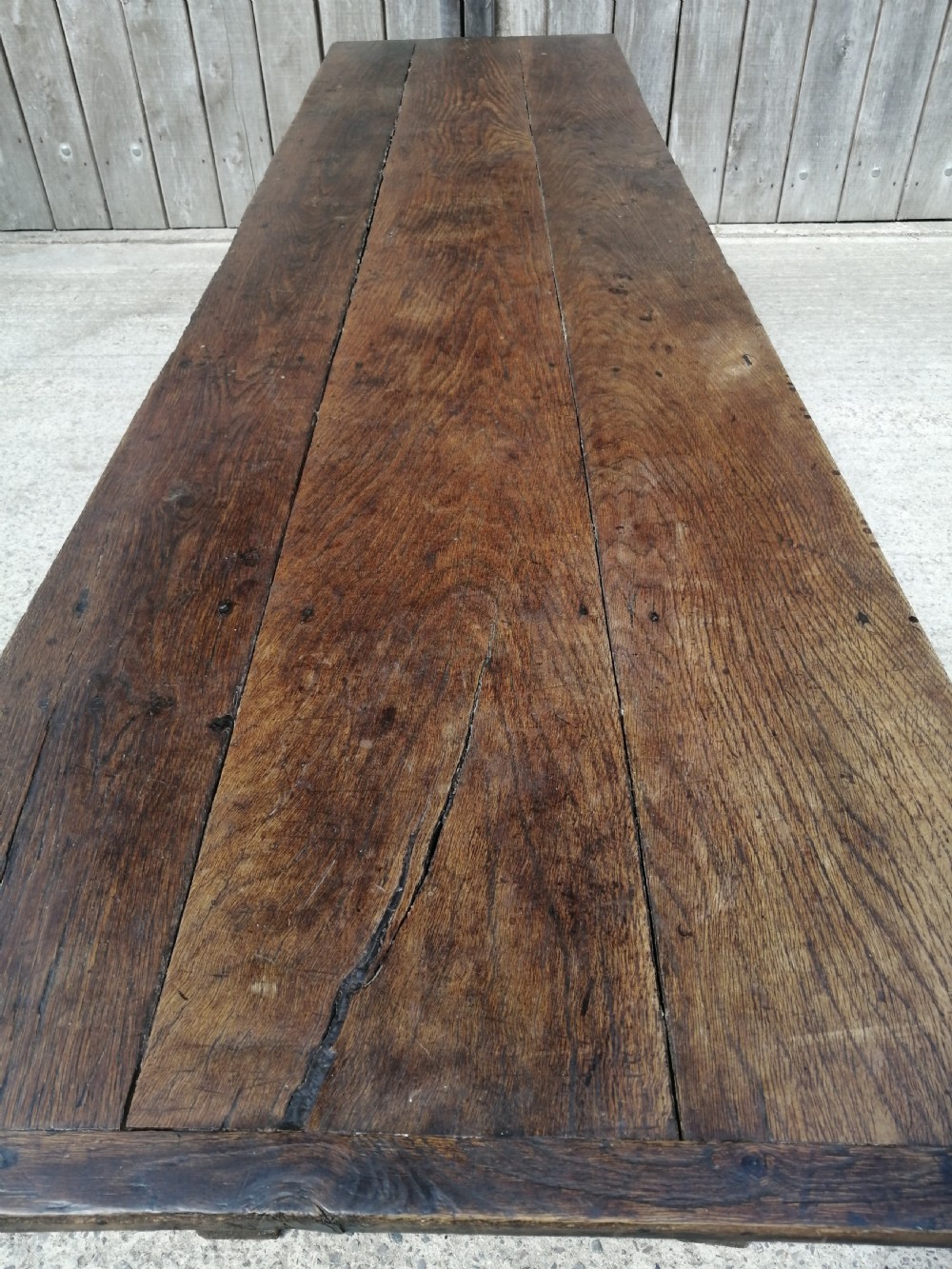 An early eighteenth-century long oak and elm refectory table top showing four wide wooden planks with natural grain, splits, and deep dark patination. View IX
