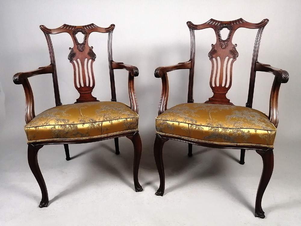 A pair of late Victorian mahogany elbow chairs featuring carved lyre back splats, curved arms, cabriole legs, and gold patterned upholstered seats.