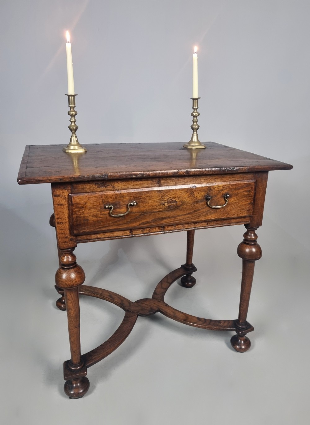 A Queen Anne period oak and elm lowboy featuring a single drawer with brass drop handles, turned legs, and a curved X-frame stretcher.