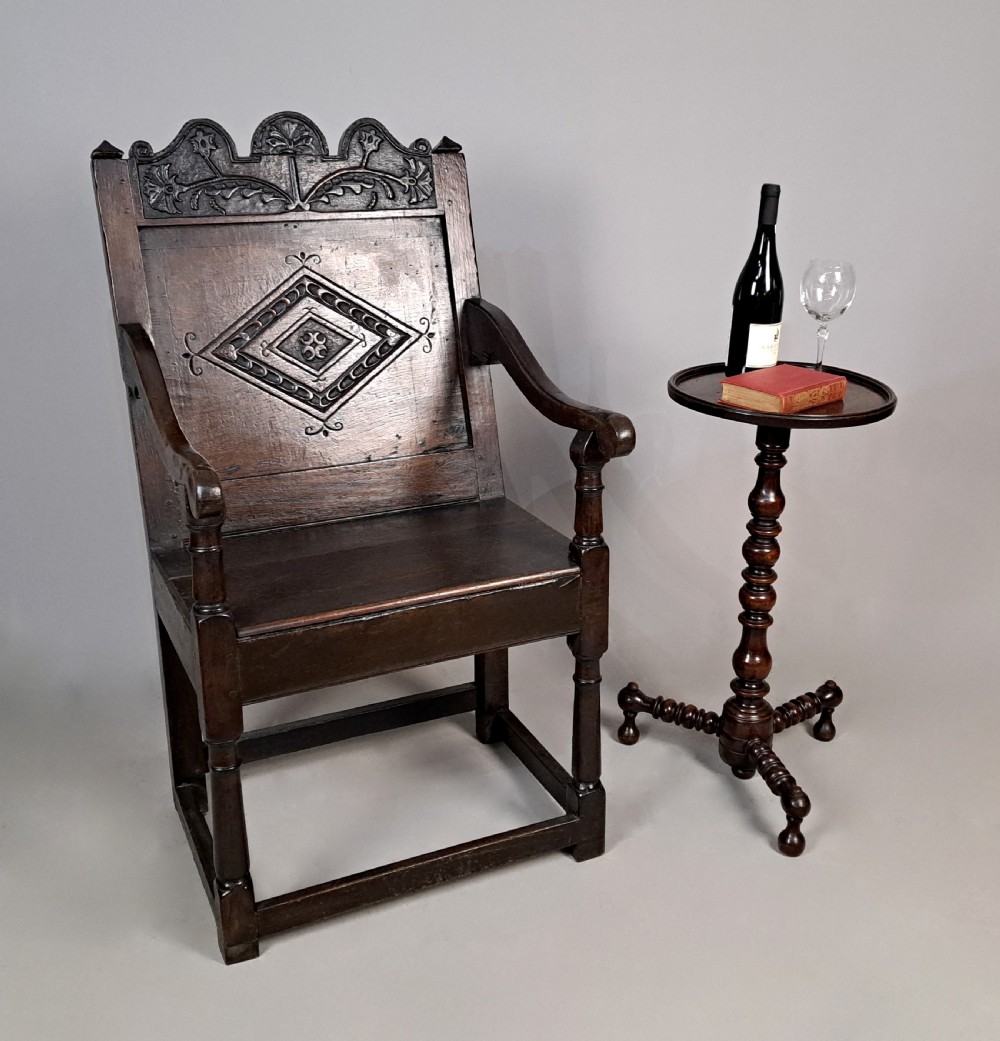 A dark oak wainscot armchair featuring a carved lozenge motif on the back panel, shaped cresting rail, shaped armrests, and turned front legs with lower stretchers. View II