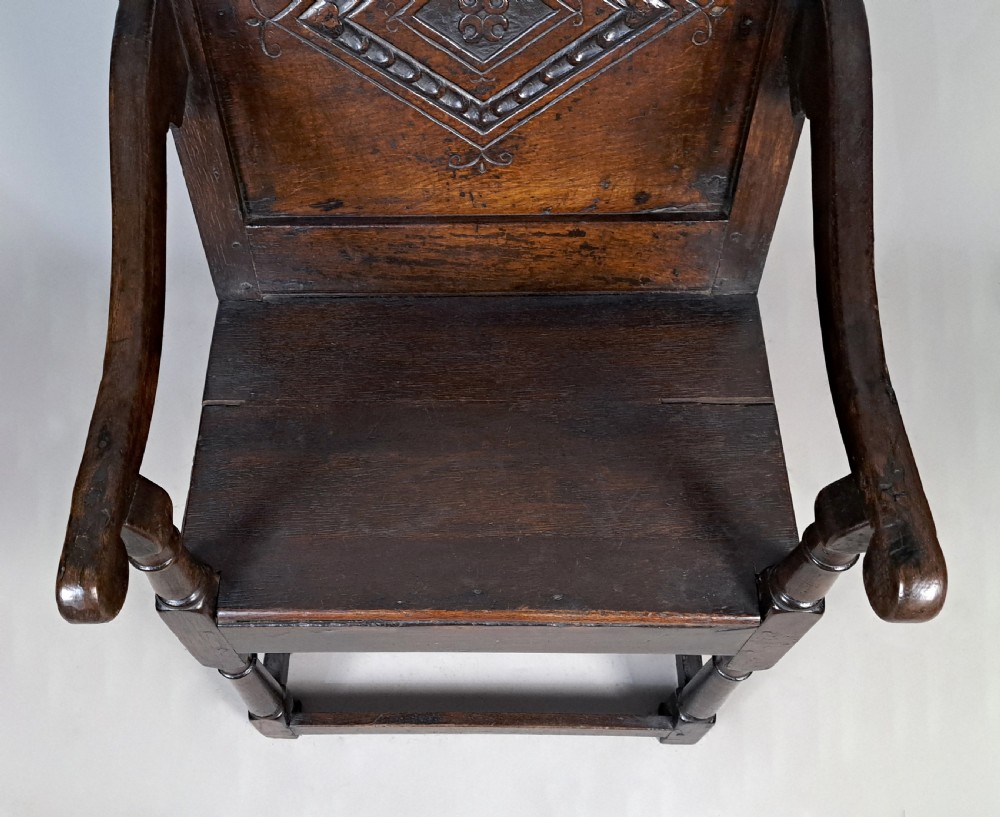 A dark oak wainscot armchair featuring a carved lozenge motif on the back panel, shaped cresting rail, shaped armrests, and turned front legs with lower stretchers. View IV