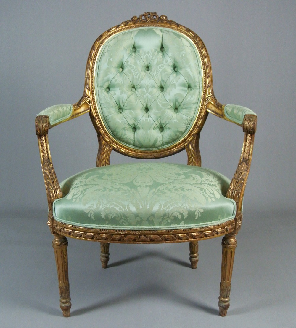 An 18th-century George III giltwood armchair featuring a button-tufted oval back rest upholstered in light green damask fabric with carved gold leaf detail.