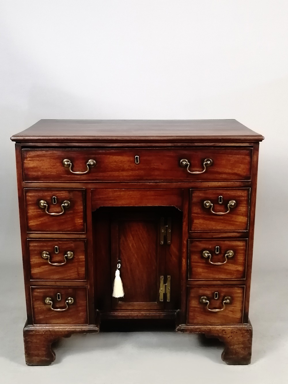A mid-18th century George II mahogany kneehole desk featuring a long top drawer over six side drawers and a central recessed cupboard on bracket feet.