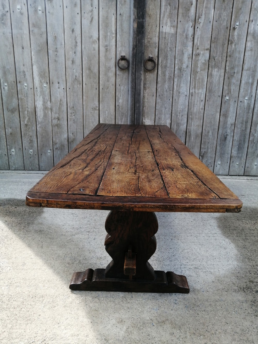 An early nineteenth-century solid elm refectory dining table with a thick plank top and a central carved trestle support.
