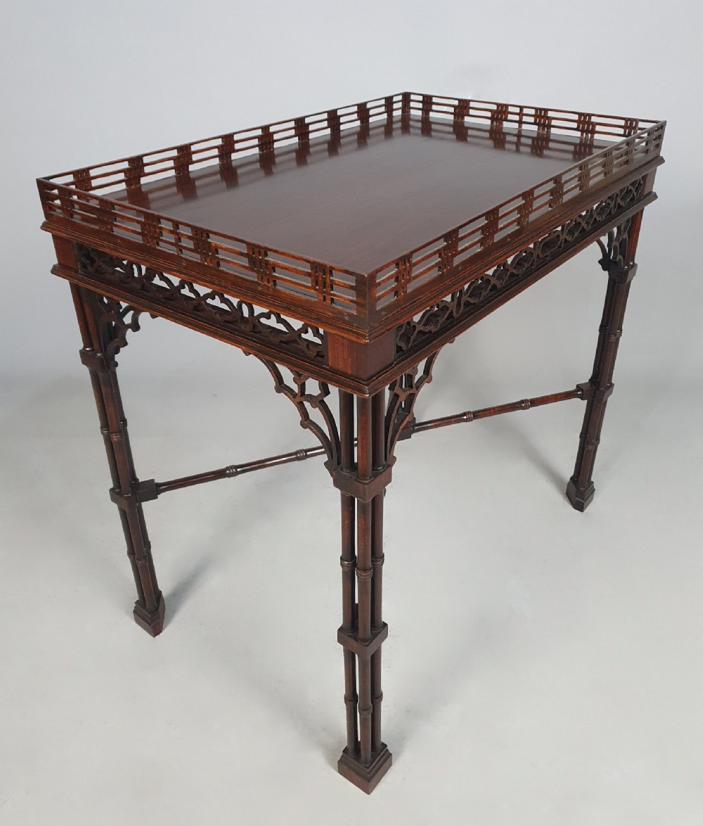 A dark padauk Chippendale style silver table featuring a pierced gallery rim, fretwork frieze, cluster legs, and turned stretchers.