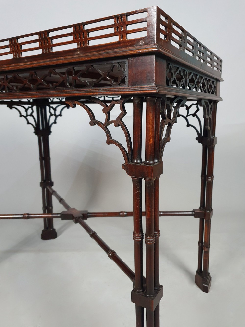 A dark padauk Chippendale style silver table featuring a pierced gallery rim, fretwork frieze, cluster legs, and turned stretchers. View VI
