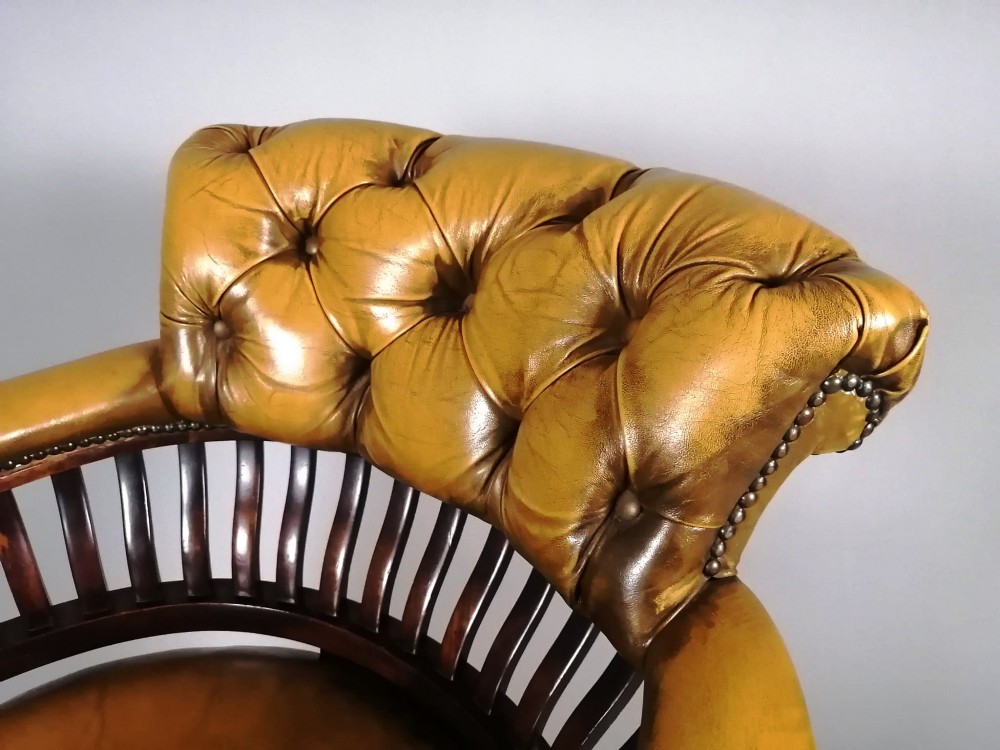 A late Victorian revolving desk chair featuring mustard tan buttoned leather upholstery, brass studding, a mahogany spindle-back frame, and turned legs on castors. View II