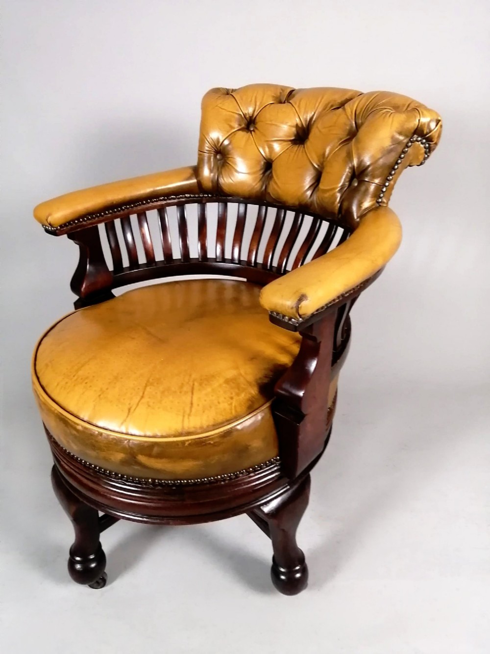 A late Victorian revolving desk chair featuring mustard tan buttoned leather upholstery, brass studding, a mahogany spindle-back frame, and turned legs on castors. View III