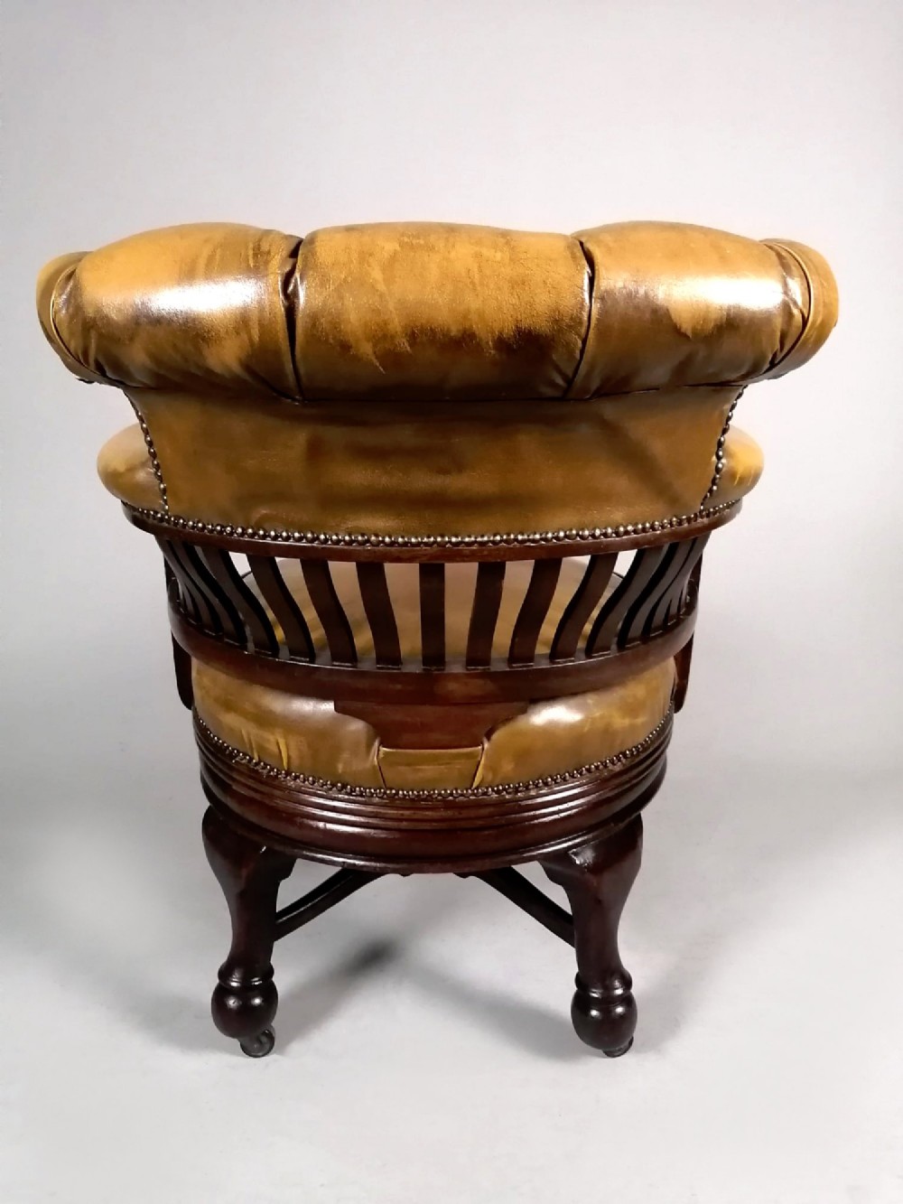 A late Victorian revolving desk chair featuring mustard tan buttoned leather upholstery, brass studding, a mahogany spindle-back frame, and turned legs on castors. View VII