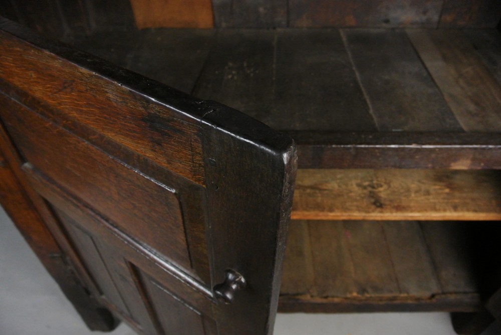An 18th-century dark oak court cupboard featuring a carved date of 1723, upper recessed cabinet with drop finials, and fielded lower door panels. View VI