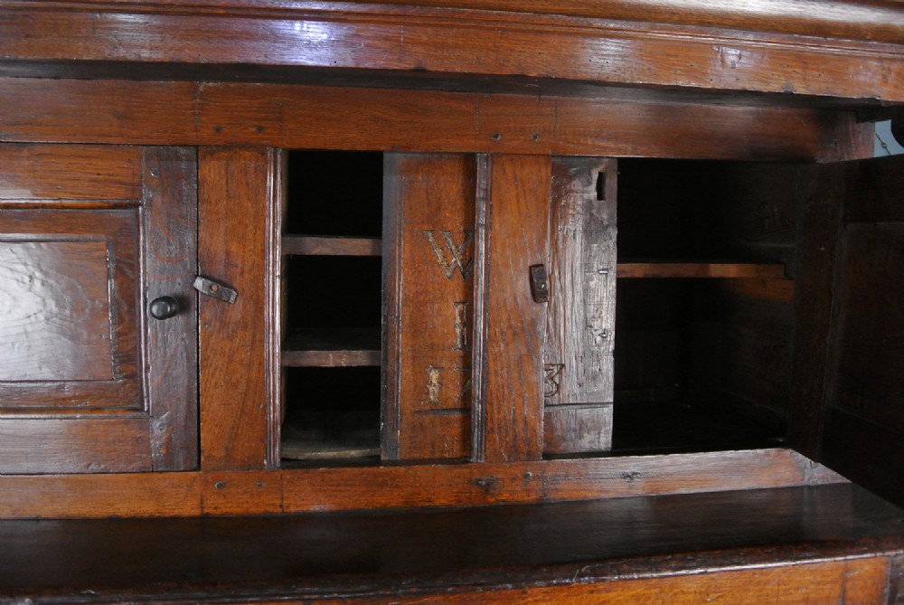 An 18th-century dark oak court cupboard featuring a carved date of 1723, upper recessed cabinet with drop finials, and fielded lower door panels. View VII