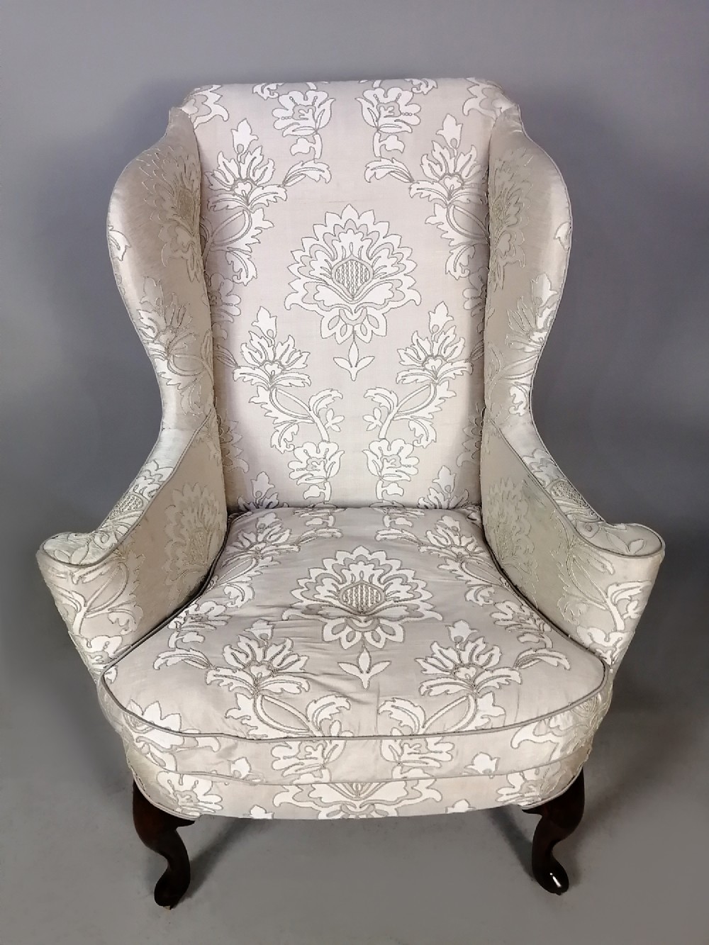 A 19th-century English wingback armchair upholstered in cream damask fabric with dark carved walnut cabriole front legs. View IV