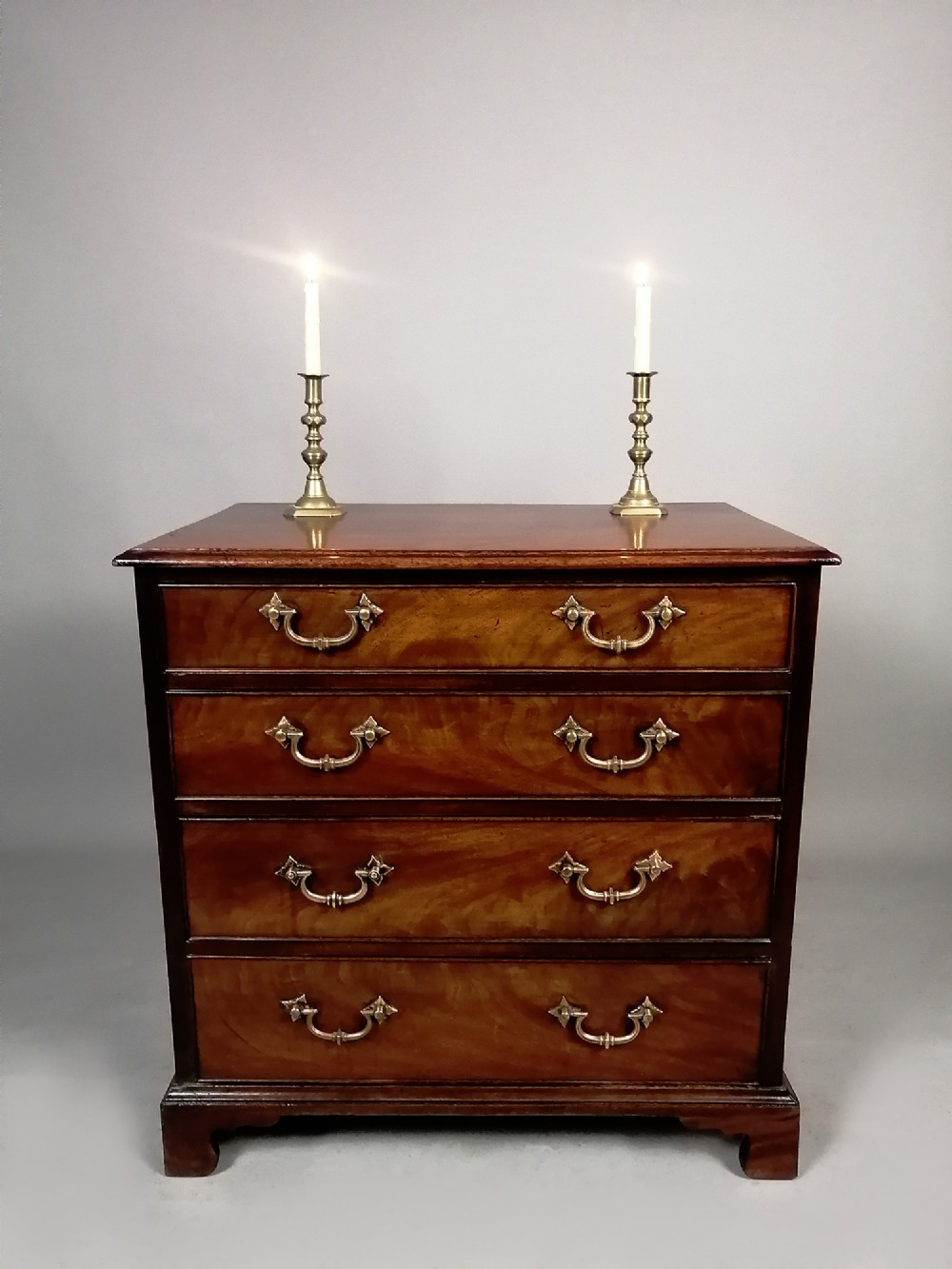 A compact George III Cuban mahogany chest of drawers featuring four graduated drawers with brass swan-neck handles and bracket feet. View IV