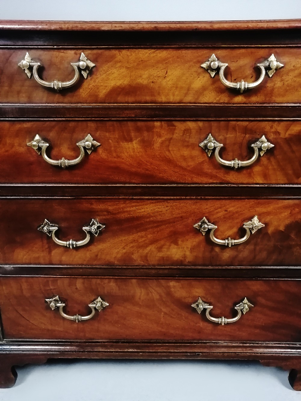 A compact George III Cuban mahogany chest of drawers featuring four graduated drawers with brass swan-neck handles and bracket feet. View VII