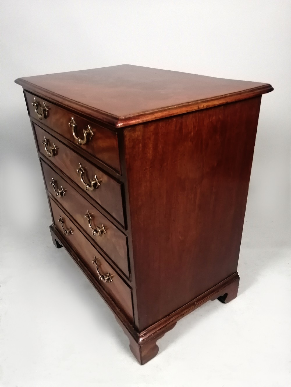 A compact George III Cuban mahogany chest of drawers featuring four graduated drawers with brass swan-neck handles and bracket feet. View VIII