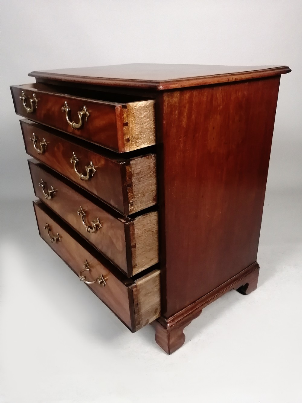 A compact George III Cuban mahogany chest of drawers featuring four graduated drawers with brass swan-neck handles and bracket feet. View IX