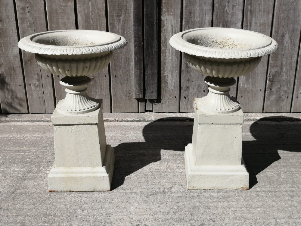 A pair of off-white painted cast iron garden urns with fluted rims and bases set upon matching square plinth pedestals.