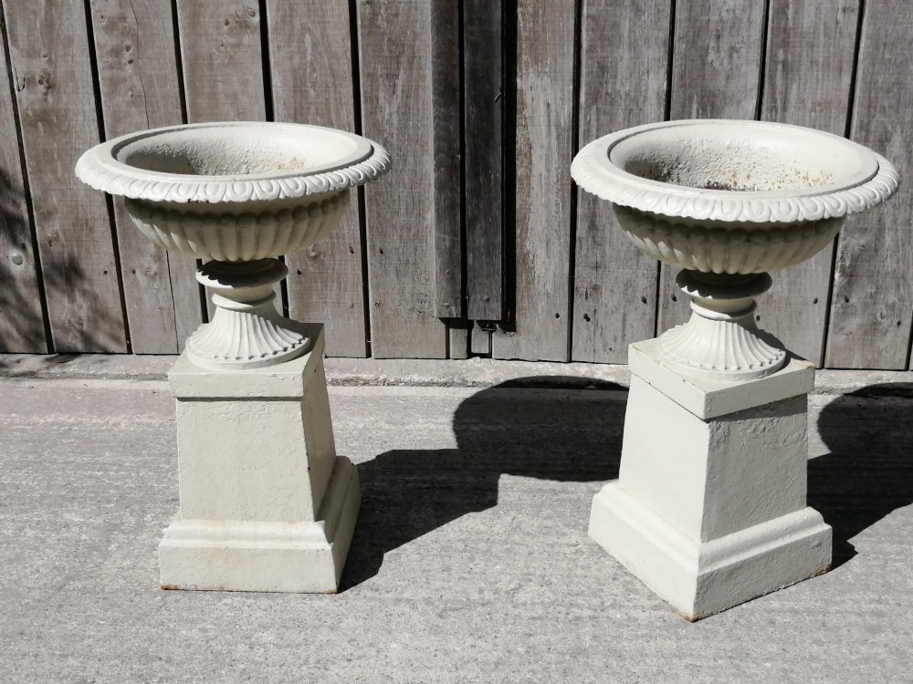 A pair of off-white painted cast iron garden urns with fluted rims and bases set upon matching square plinth pedestals. View II