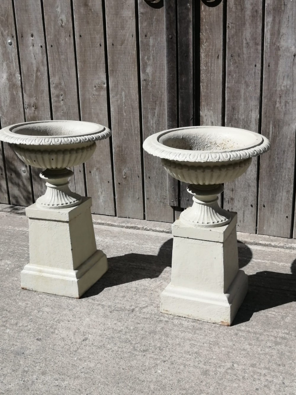 A pair of off-white painted cast iron garden urns with fluted rims and bases set upon matching square plinth pedestals. View III