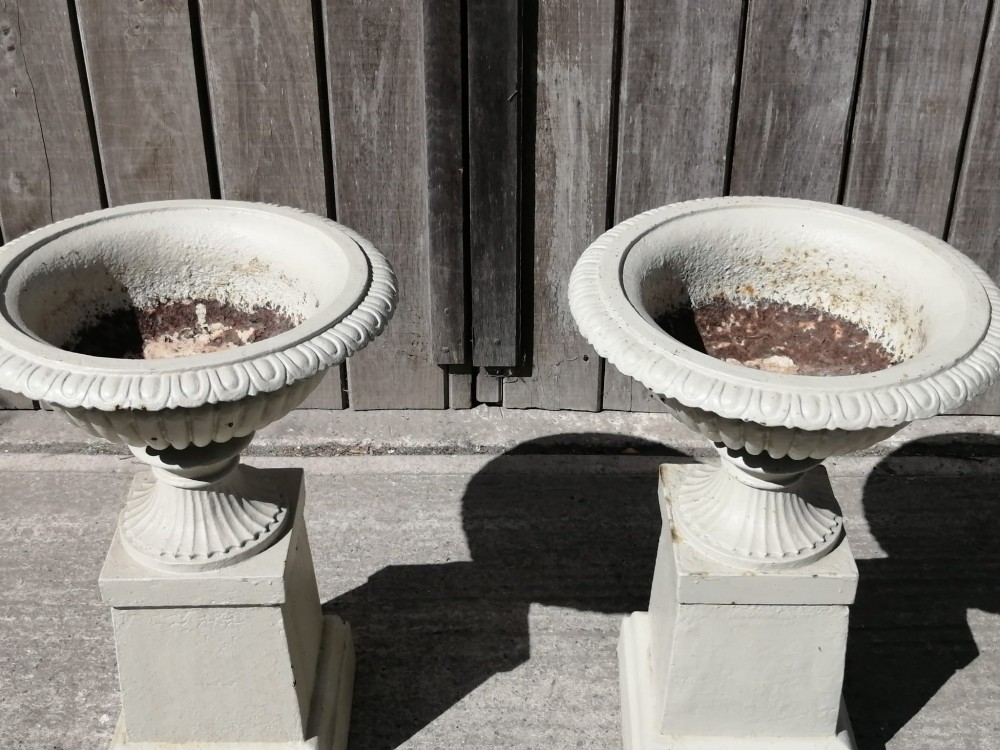 A pair of off-white painted cast iron garden urns with fluted rims and bases set upon matching square plinth pedestals. View V