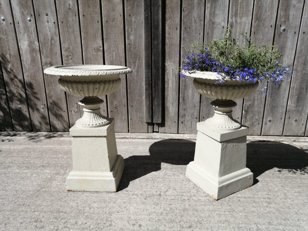 A pair of off-white painted cast iron garden urns with fluted rims and bases set upon matching square plinth pedestals. View VI