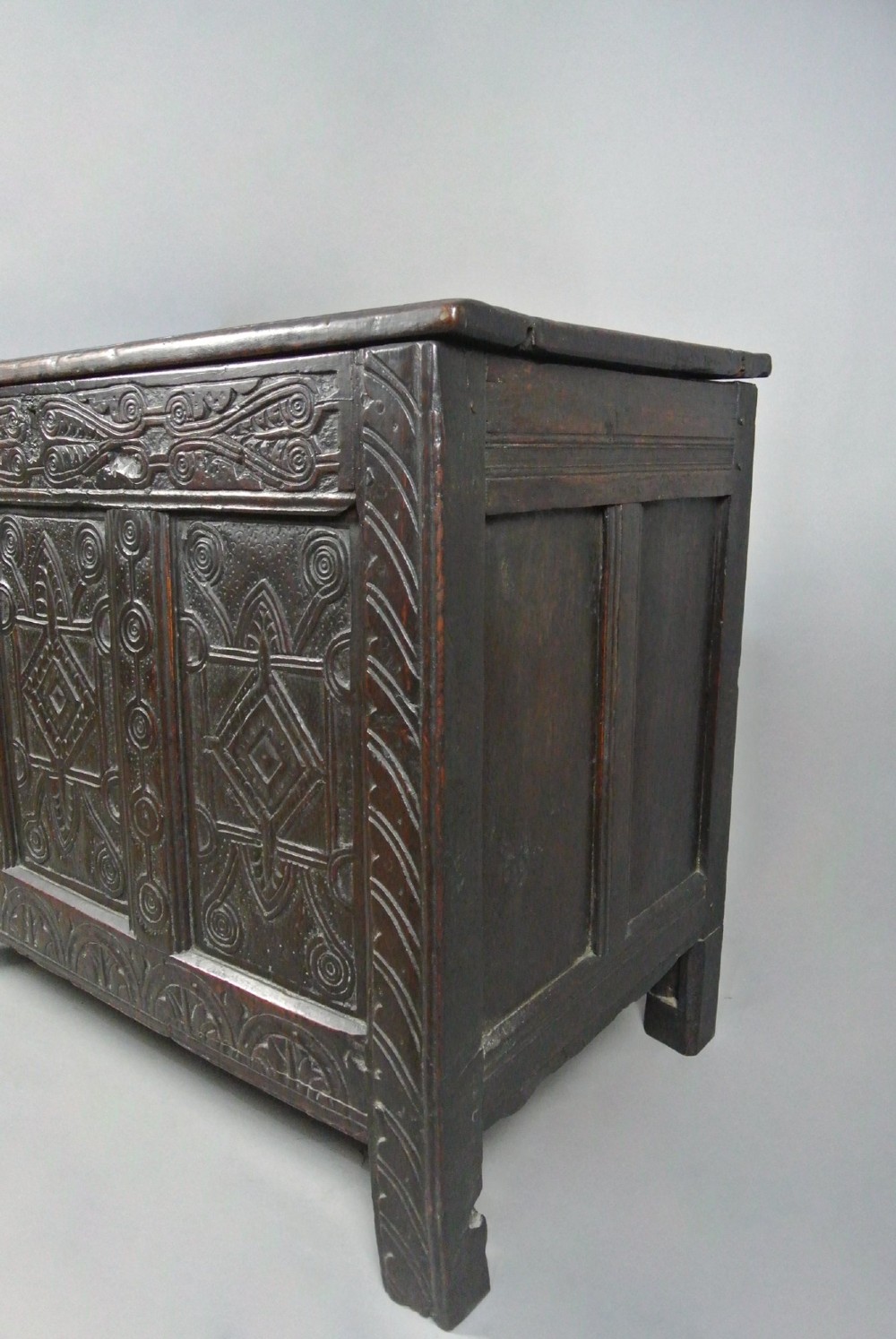 A dark oak Jacobean coffer featuring three carved front panels with diamond and circle motifs, a lunette carved top rail, and stile legs. View V