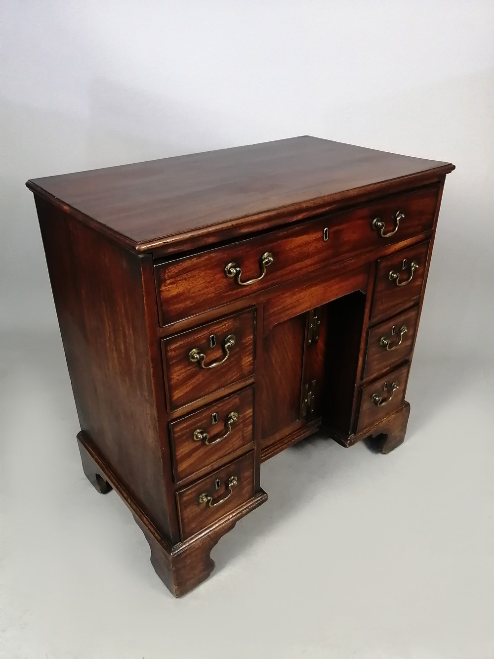 An 18th-century Georgian mahogany kneehole desk featuring multiple drawers with brass handles, bracket feet, and a central cupboard door. View IV