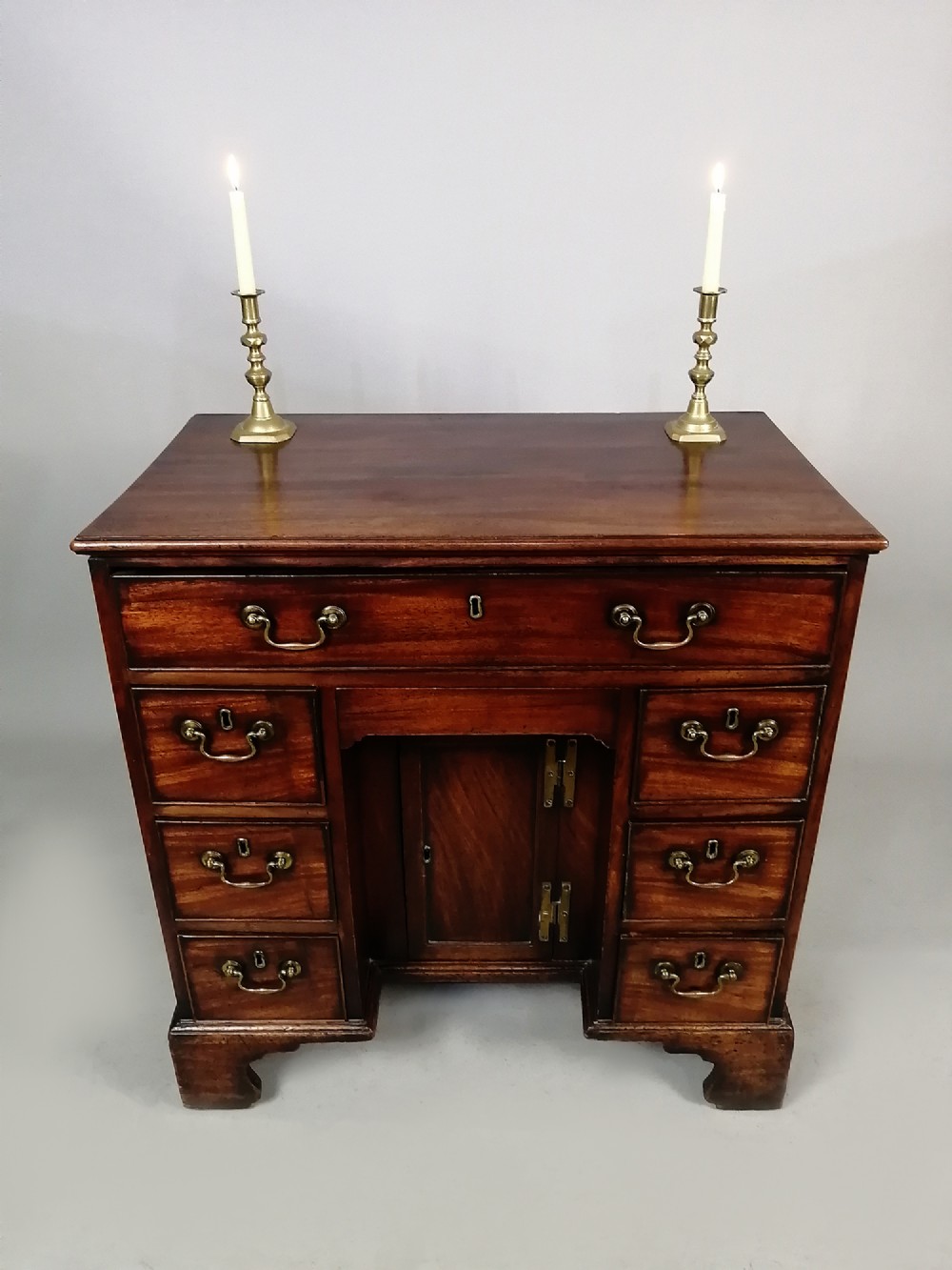 An 18th-century Georgian mahogany kneehole desk featuring multiple drawers with brass handles, bracket feet, and a central cupboard door. View V