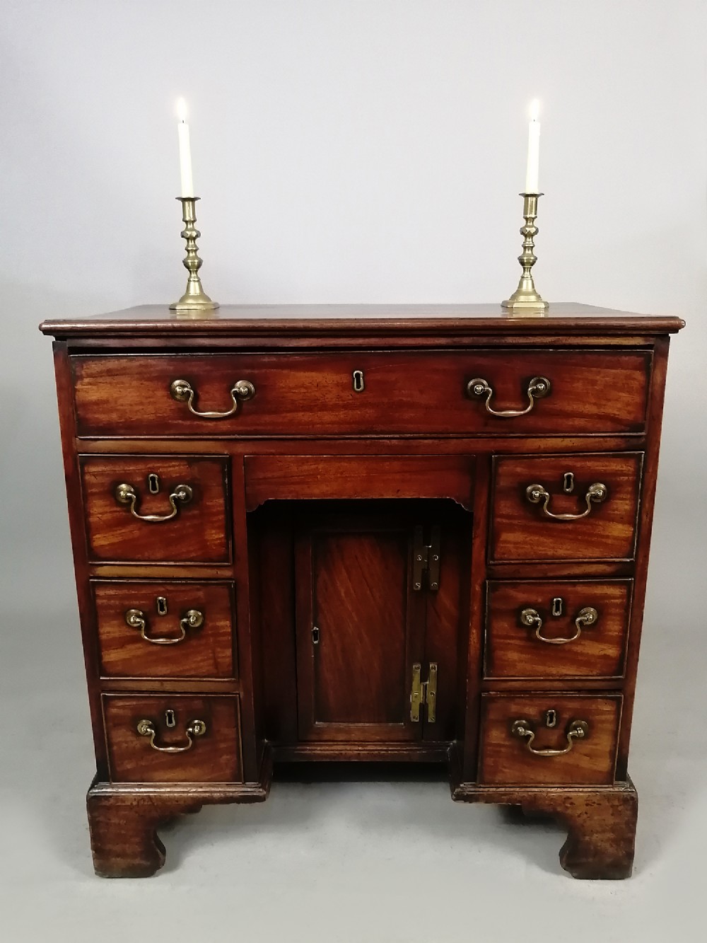 An 18th-century Georgian mahogany kneehole desk featuring multiple drawers with brass handles, bracket feet, and a central cupboard door. View VI