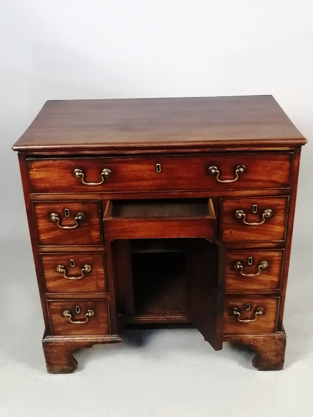 An 18th-century Georgian mahogany kneehole desk featuring multiple drawers with brass handles, bracket feet, and a central cupboard door. View VII