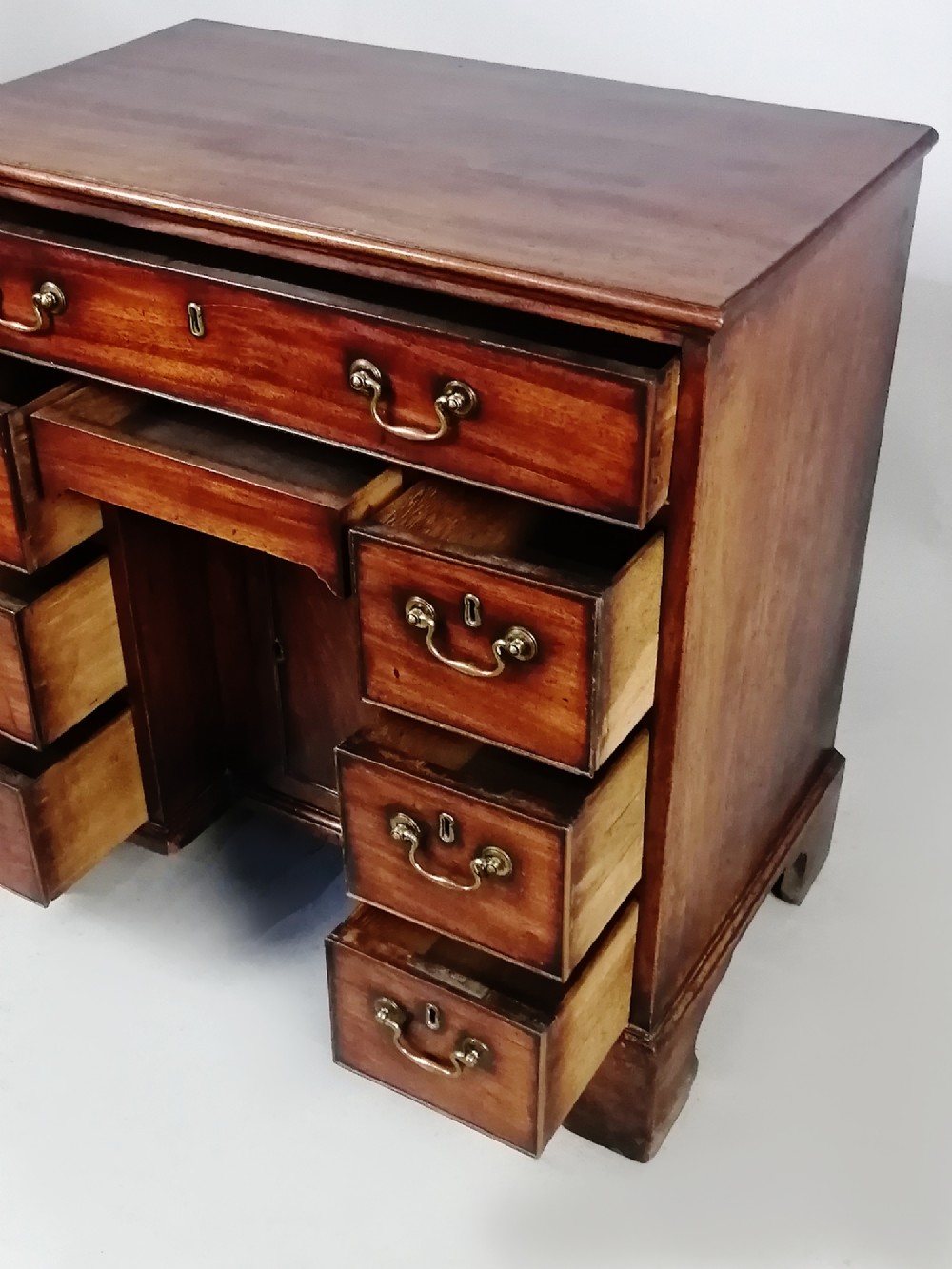 An 18th-century Georgian mahogany kneehole desk featuring multiple drawers with brass handles, bracket feet, and a central cupboard door. View VIII