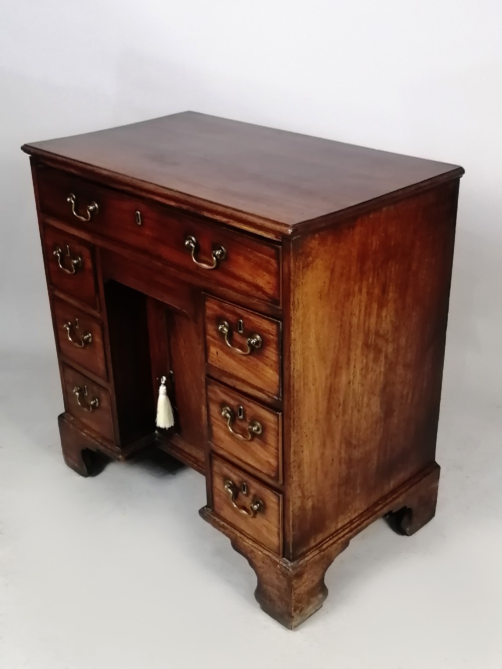 An 18th-century Georgian mahogany kneehole desk featuring multiple drawers with brass handles, bracket feet, and a central cupboard door. View IX