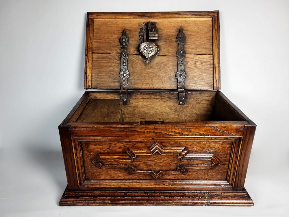 An open seventeenth-century oak safe box featuring raised geometric mouldings on the front panel and a hand-forged steel lock plate inside the lid.