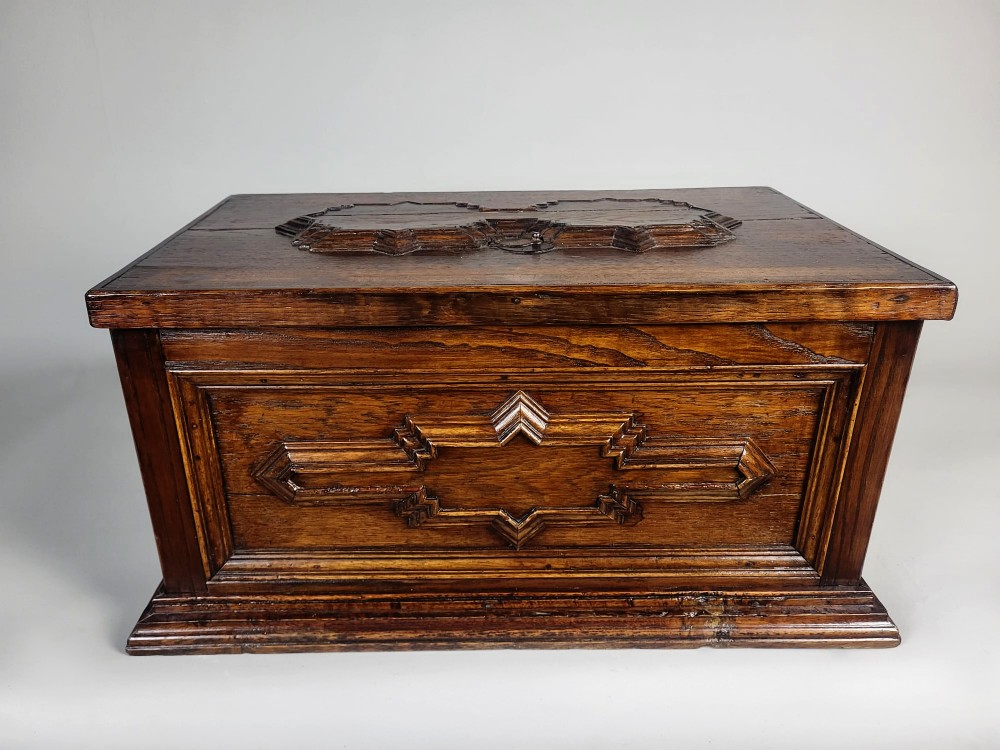 An open seventeenth-century oak safe box featuring raised geometric mouldings on the front panel and a hand-forged steel lock plate inside the lid. View II