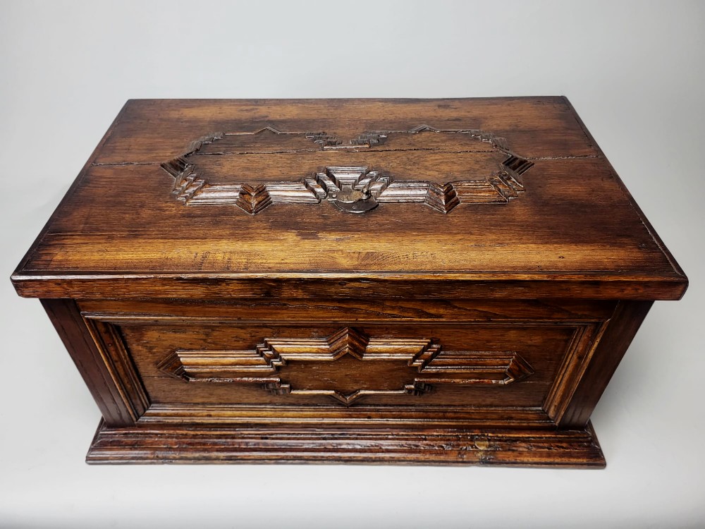 An open seventeenth-century oak safe box featuring raised geometric mouldings on the front panel and a hand-forged steel lock plate inside the lid. View V