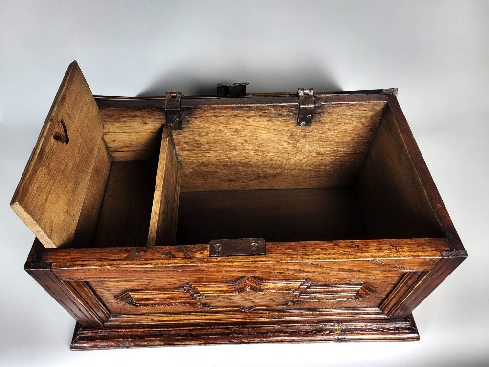 An open seventeenth-century oak safe box featuring raised geometric mouldings on the front panel and a hand-forged steel lock plate inside the lid. View VI