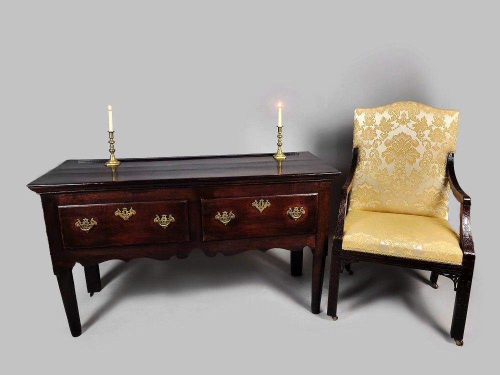 A George III dark oak dresser base featuring two drawers with ornate brass handles and escutcheons, a shaped apron, and tapered legs. View II