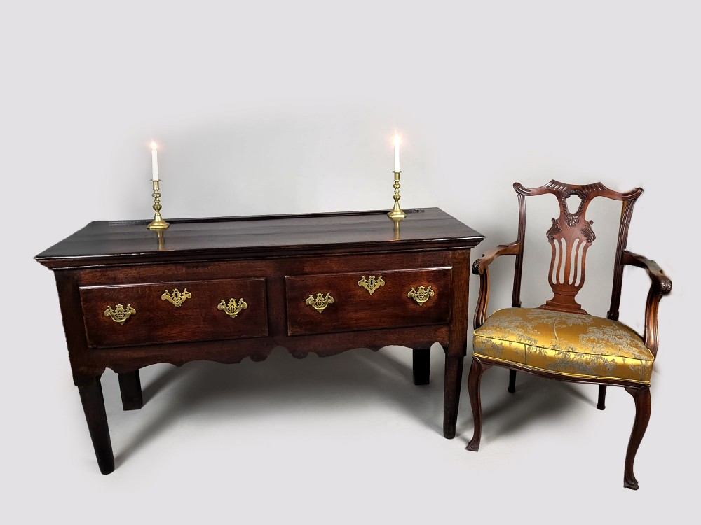 A George III dark oak dresser base featuring two drawers with ornate brass handles and escutcheons, a shaped apron, and tapered legs. View III