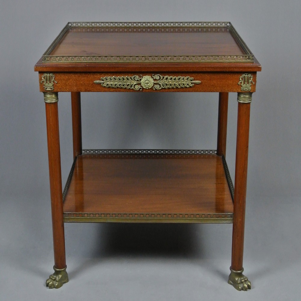 A two-tiered Regency mahogany centre table featuring pierced brass gallery rims, decorative brass frieze mounts, cylindrical columns, and cast brass paw feet.