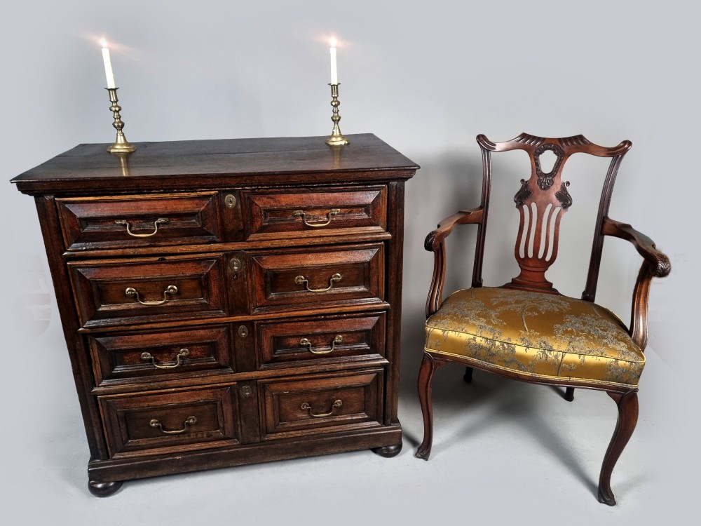 A seventeenth-century dark oak chest of drawers featuring geometric mitred drawer panels, brass swing handles, and turned bun feet. View II
